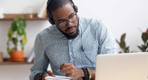 Focused,African,Business,Man,In,Headphones,Writing,Notes,In,Notebook